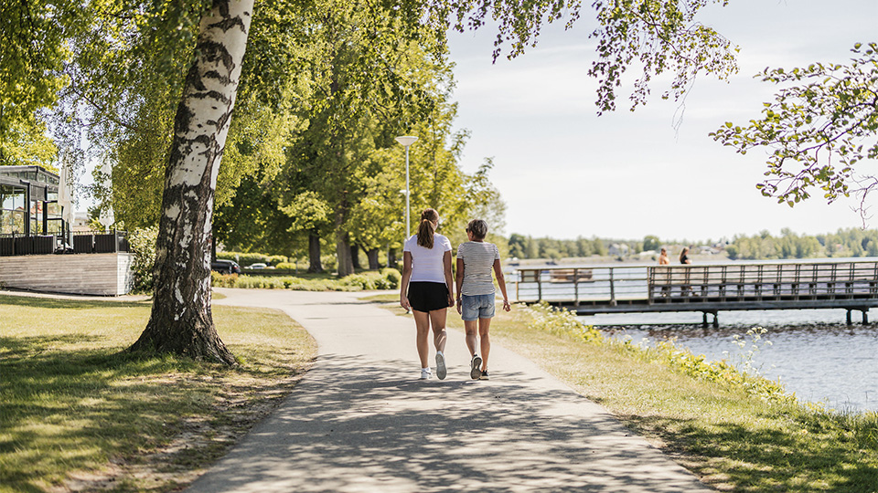 Kvinna och flicka som går på cykelväg längs med strandpromenaden i Lindesberg, en del av Lindessjön runt. 