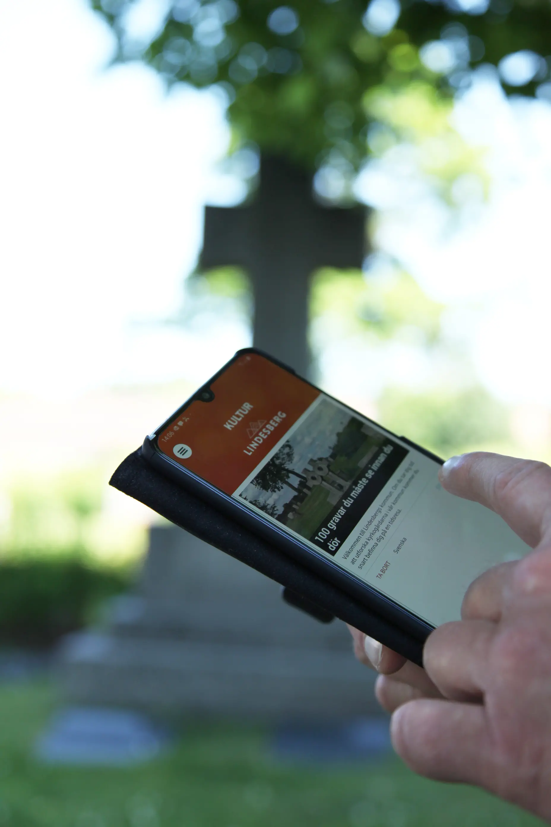 En hand som håller i en telefon som visar den digitala guiden 100 gravar du behöver se innan du dör.